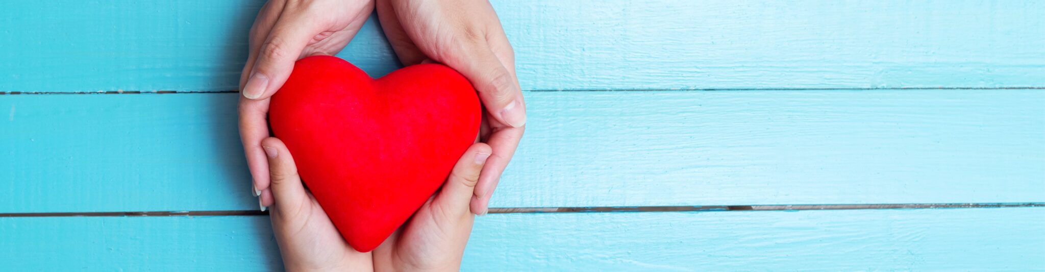 two hands holding a red heart over a blue wood background